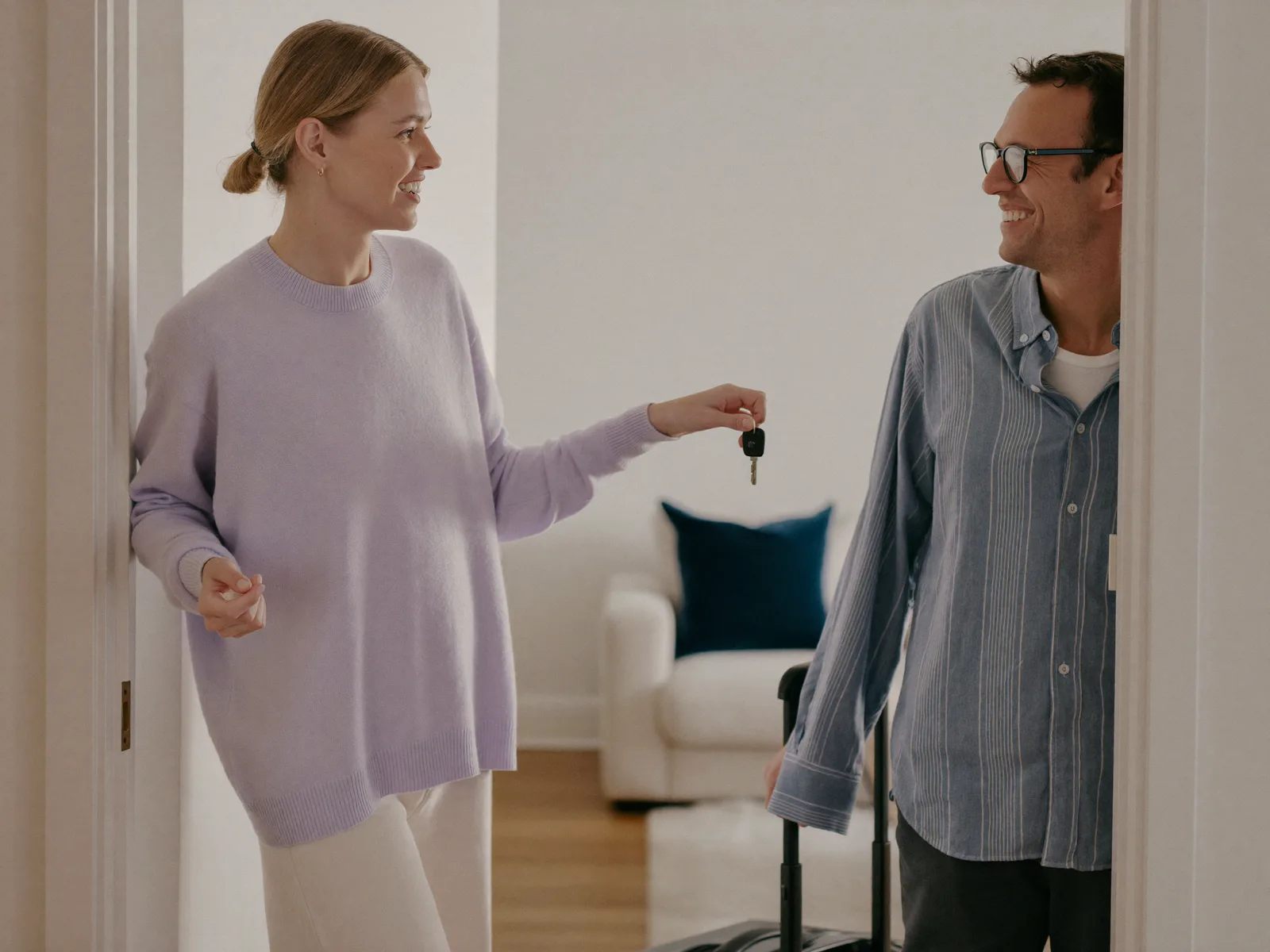 A host handing door keys to a guest with a suitcase in the doorway of a bright flat